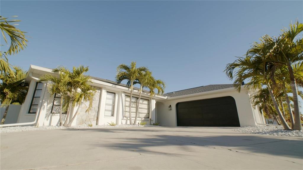 A white single-story house with a black garage door and palm trees in the front yard — 18770 MCGRATH CIRCLE, PORT CHARLOTTE, FL