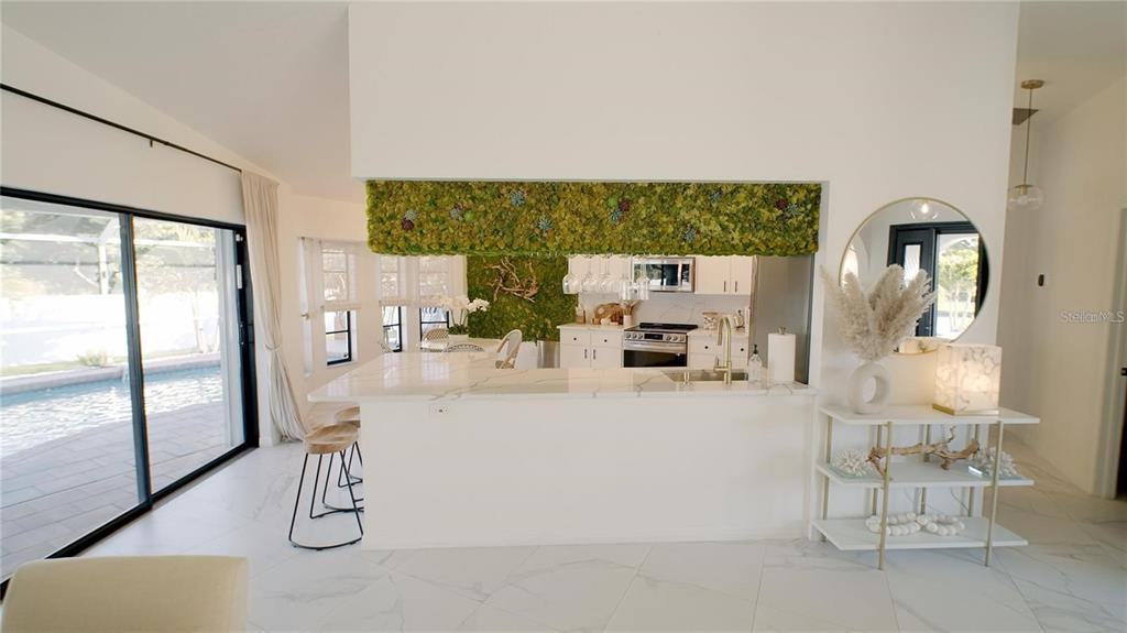 A kitchen with a moss-covered accent wall, white countertops, and a view of a pool — 18770 MCGRATH CIRCLE, PORT CHARLOTTE, FL
