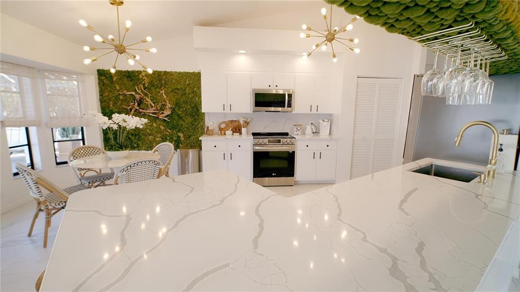 A bright kitchen features white cabinets, quartz countertops, a moss wall, and two sputnik chandeliers — 18770 MCGRATH CIRCLE, PORT CHARLOTTE, FL