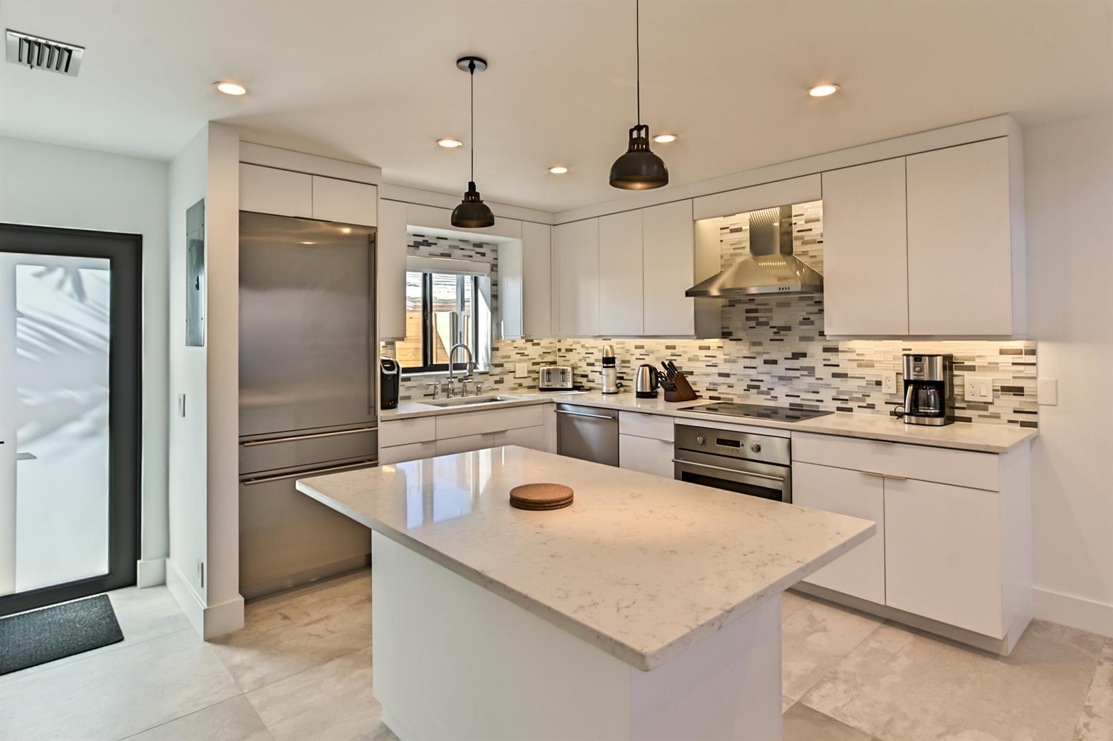 A modern kitchen features white cabinetry, stainless steel appliances, a marble-topped island, and tile backsplash — 1955 NE 4th Street Unit 2, Deerfield Beach FL 33441, DEERFIELD BEACH, FL
