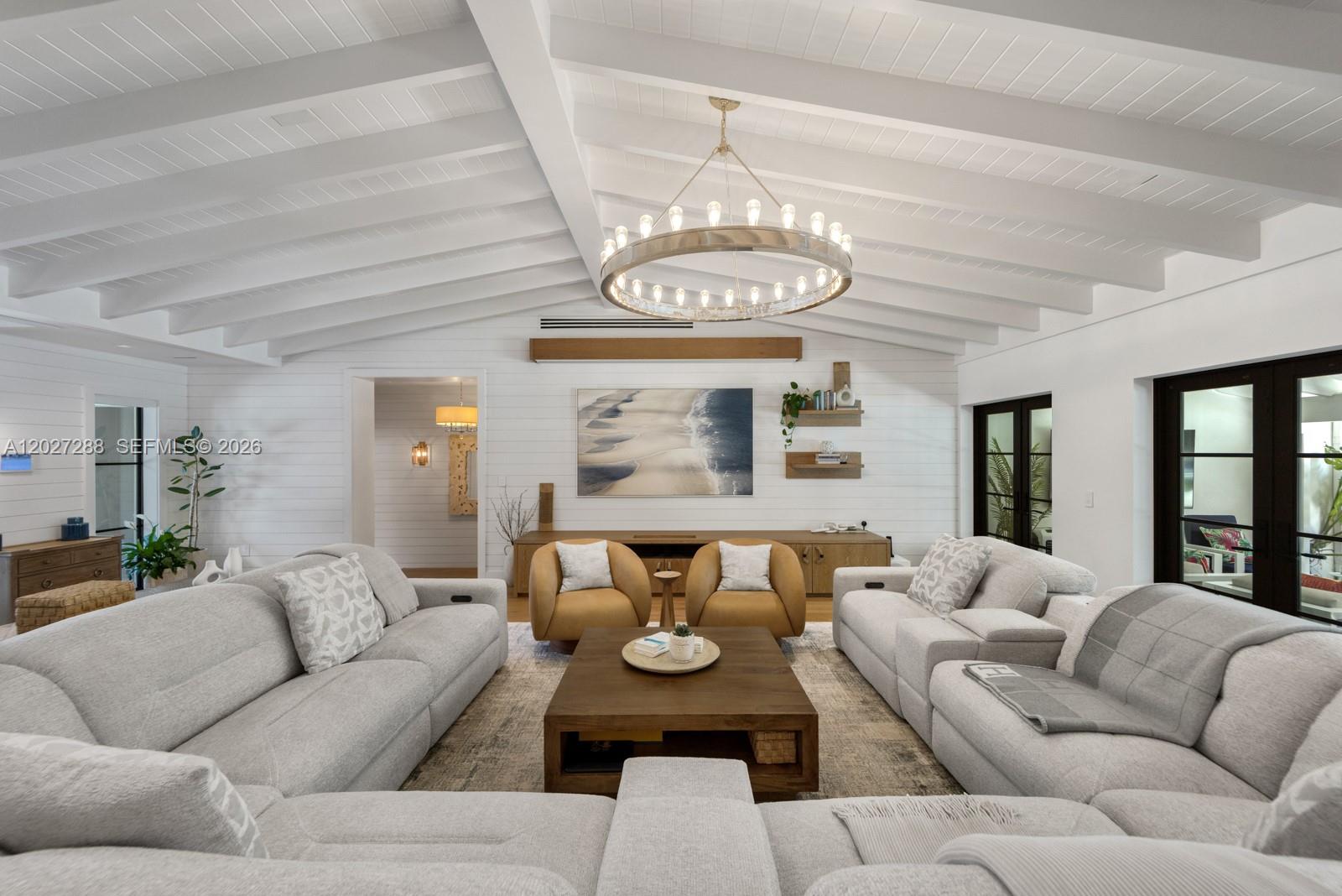 A bright living room features a vaulted beamed ceiling, a large chandelier, and neutral furniture — 7101 SW 66th St, Miami FL 33143, MIAMI, FL