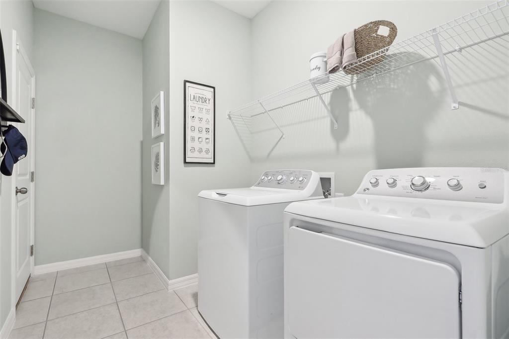 A laundry room features white appliances, a wire shelf, and a framed laundry symbol sign — 1830 AMERICAN WAY, HAINES CITY, FL