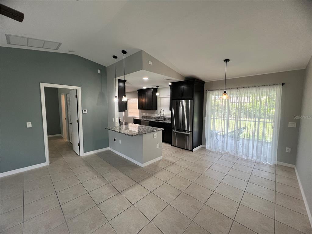 A kitchen with dark cabinets, granite countertops, and a breakfast bar opens to a dining area — 11969 XAVIER AVENUE, PORT CHARLOTTE, FL