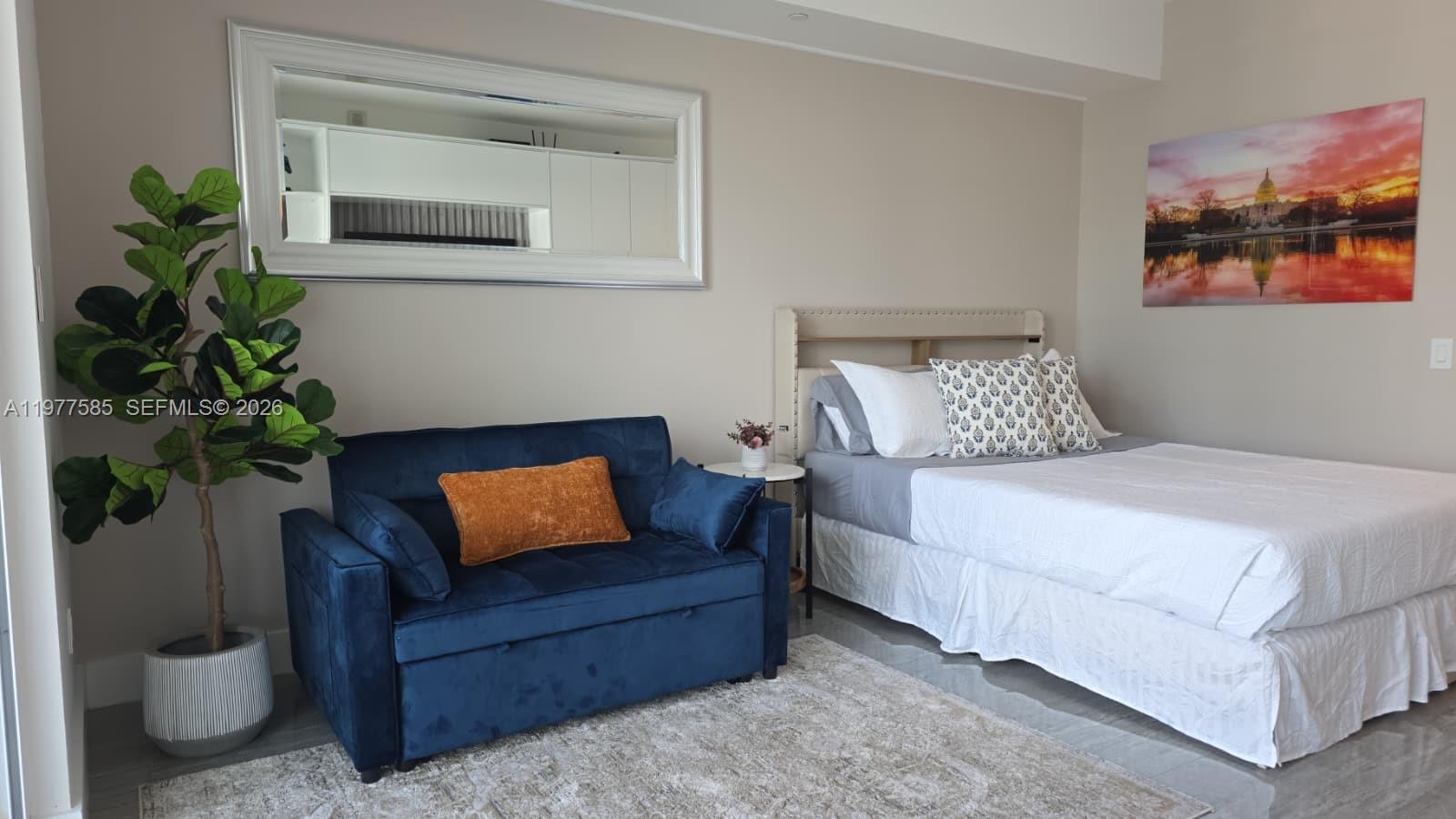 A bedroom features a blue sofa, a bed with white bedding, and a large wall mirror — 1300 Brickell Bay Dr # 2512, Miami FL 33131, MIAMI, FL