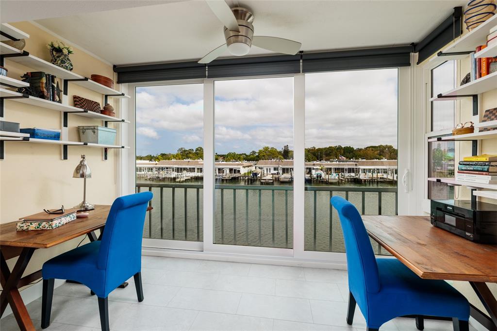 A home office with two desks, blue chairs, wall shelving, and a waterfront balcony view — 1 BOCA CIEGA POINT BOULEVARD UNIT 206, ST PETERSBURG, FL