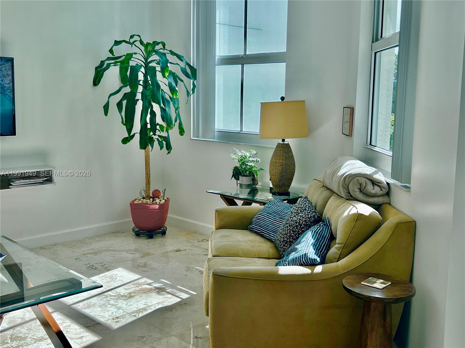 A living room features a yellow sofa, a large potted plant, and marble flooring — 9172 Collins Ave # 305, Surfside FL 33154, SURFSIDE, FL