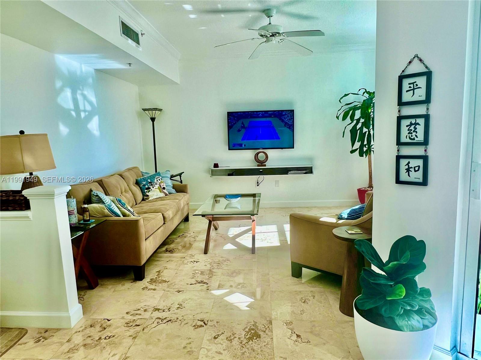 A living room features a beige sofa, glass coffee table, wall-mounted television, and tile flooring — 9172 Collins Ave # 305, Surfside FL 33154, SURFSIDE, FL