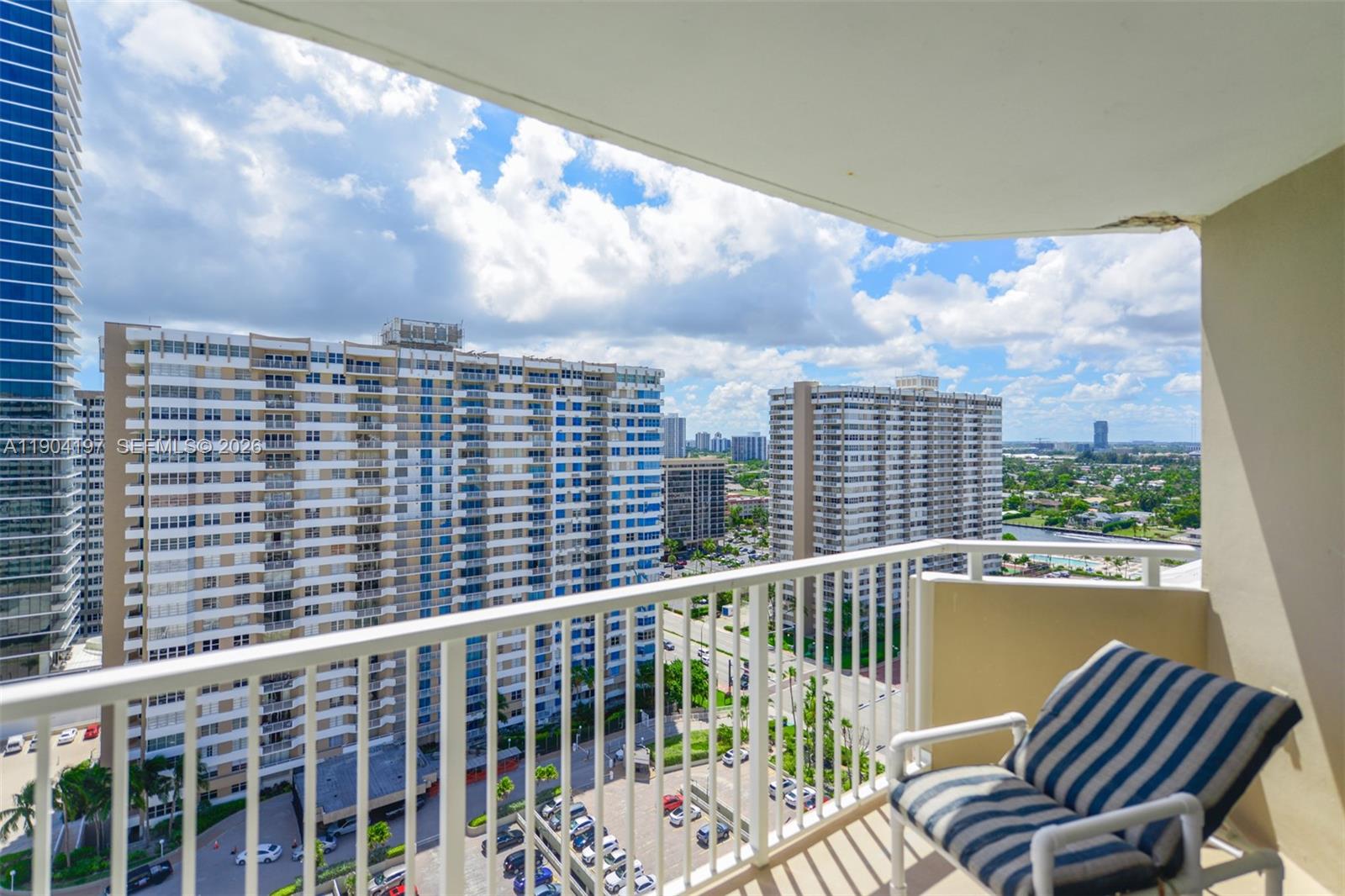A balcony with a striped chair overlooks a parking lot and tall apartment buildings — 1950 S Ocean Dr # 19A, Hallandale Beach FL 33009, HALLANDALE BEACH, FL