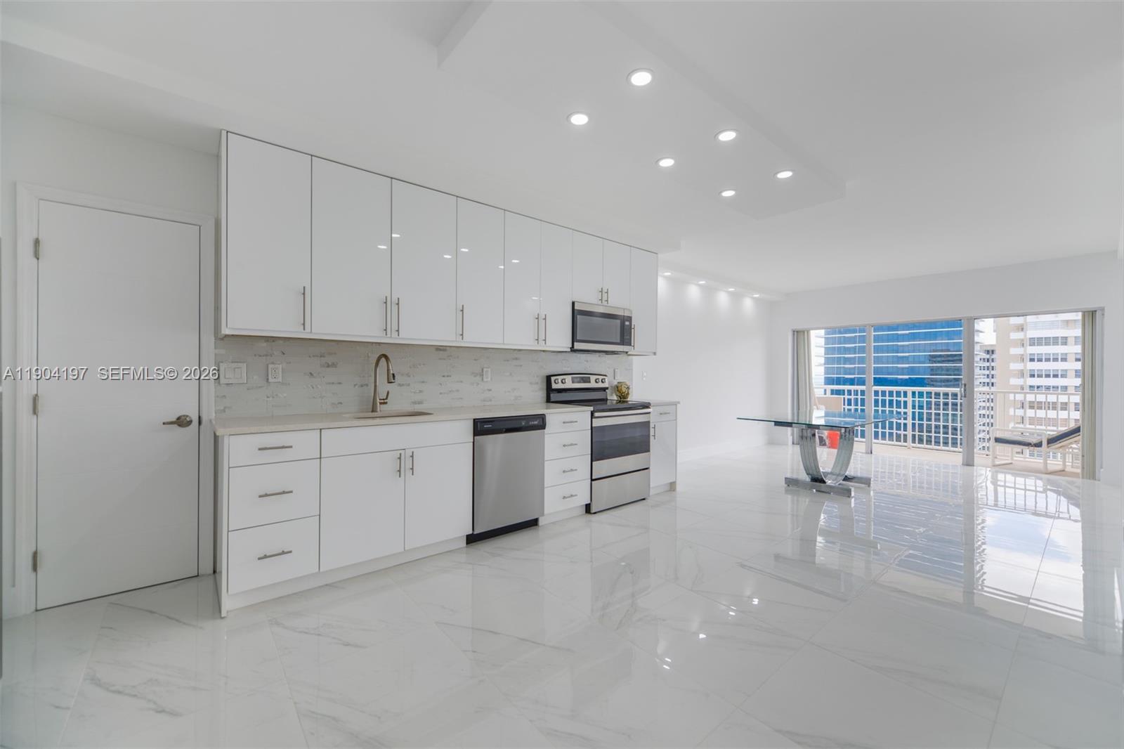 A modern white kitchen features glossy cabinets, stainless steel appliances, and marble-look tile flooring — 1950 S Ocean Dr # 19A, Hallandale Beach FL 33009, HALLANDALE BEACH, FL