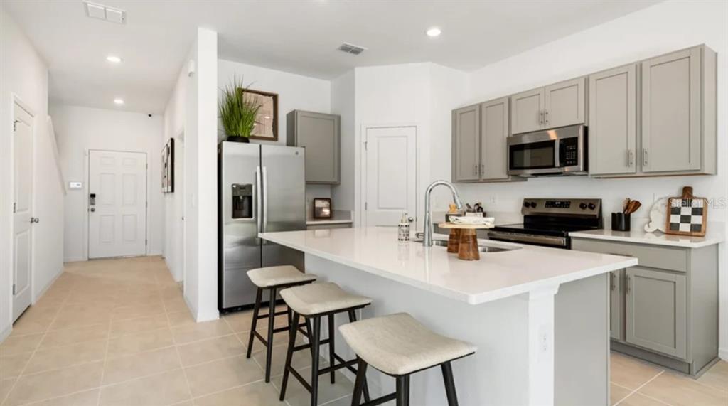 A modern kitchen features gray cabinets, a white island with bar stools, and stainless appliances — 10782 ECLIPSE STREET, SARASOTA, FL