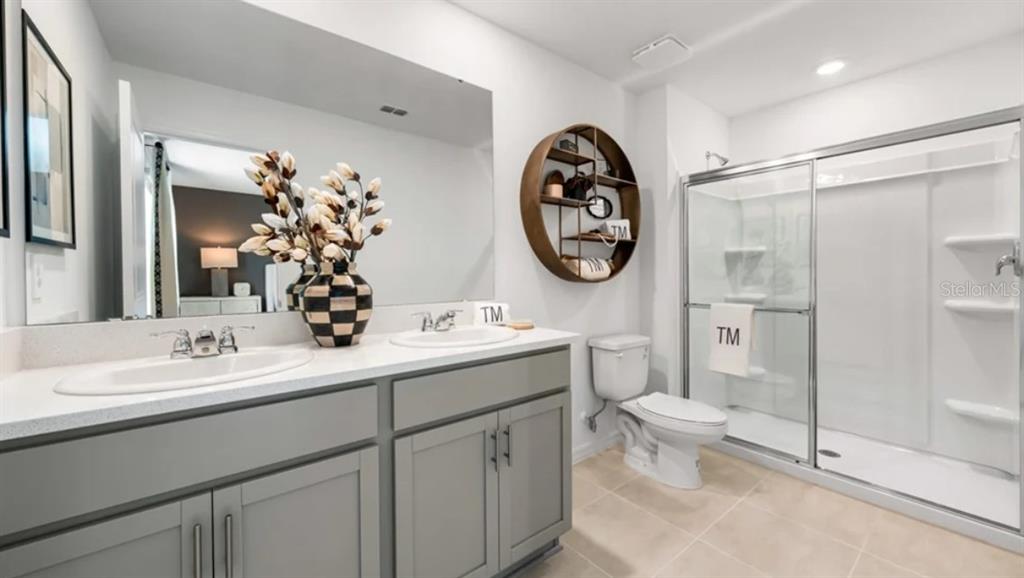 A bathroom features a double vanity with gray cabinets, a walk-in shower, and circular shelving — 10782 ECLIPSE STREET, SARASOTA, FL