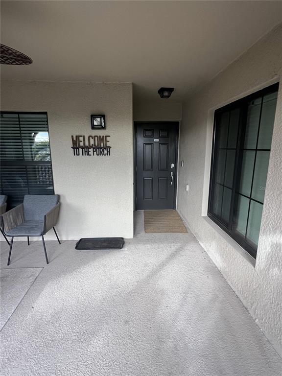 A covered porch features a dark front door, a gray chair, and a welcome sign — 5674 PALMER CIRCLE UNIT 203, BRADENTON, FL