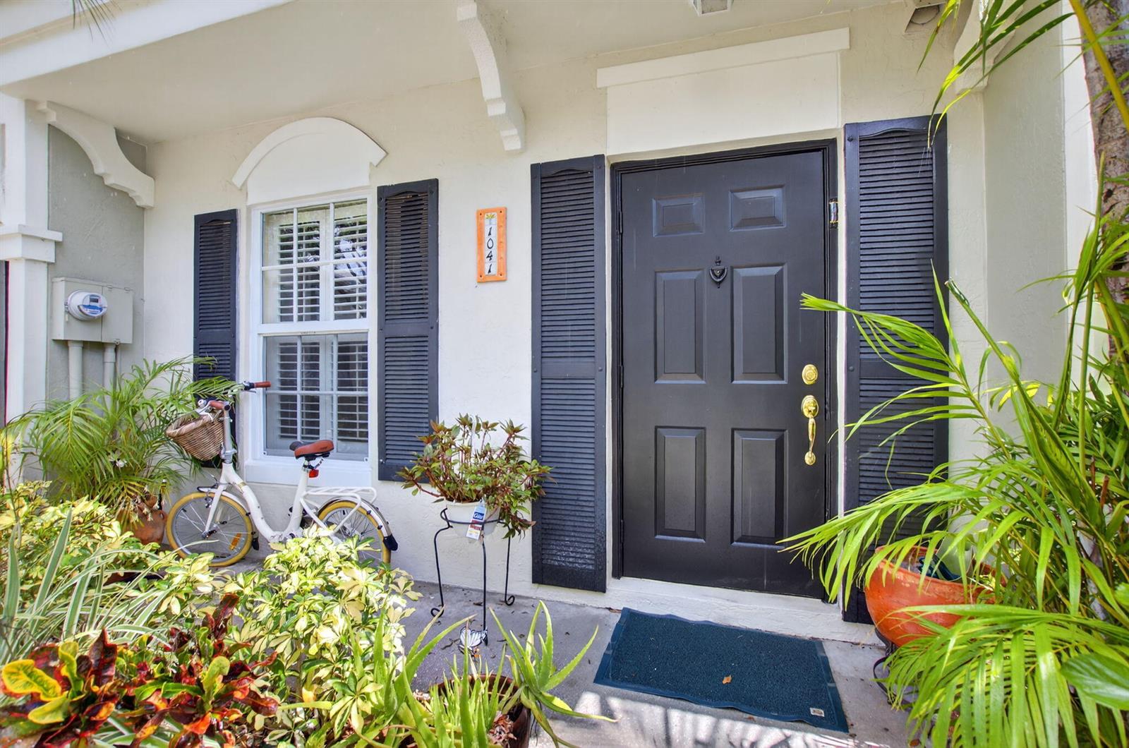 A front entryway features a black door with shutters, a bicycle, and potted plants — 1041 Kokomo Key Lane, Delray Beach FL 33483, DELRAY BEACH, FL