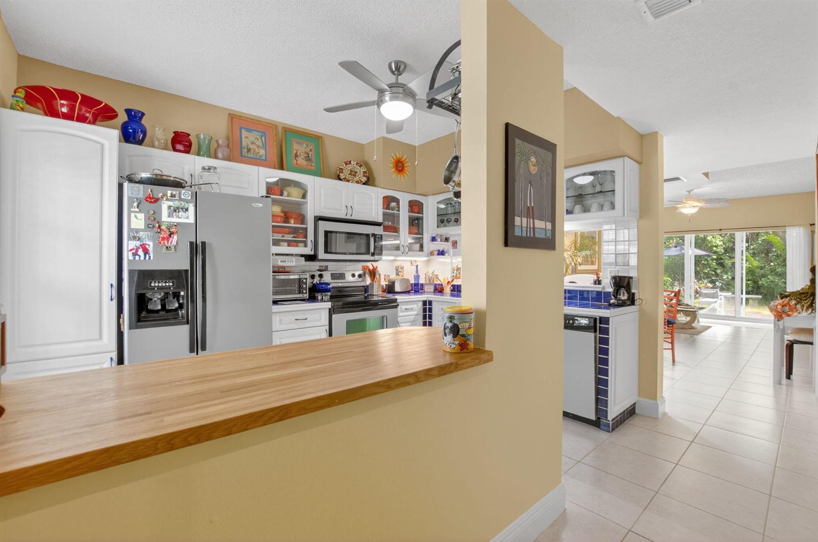 A kitchen features a wooden breakfast bar, white cabinetry, stainless steel appliances, and tile flooring — 1041 Kokomo Key Lane, Delray Beach FL 33483, DELRAY BEACH, FL