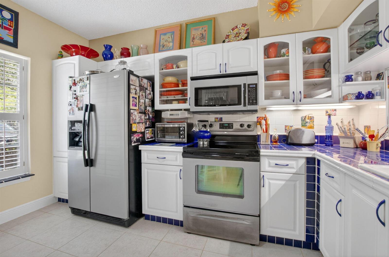 A kitchen features white cabinets, stainless steel appliances, blue tile countertops, and a window — 1041 Kokomo Key Lane, Delray Beach FL 33483, DELRAY BEACH, FL
