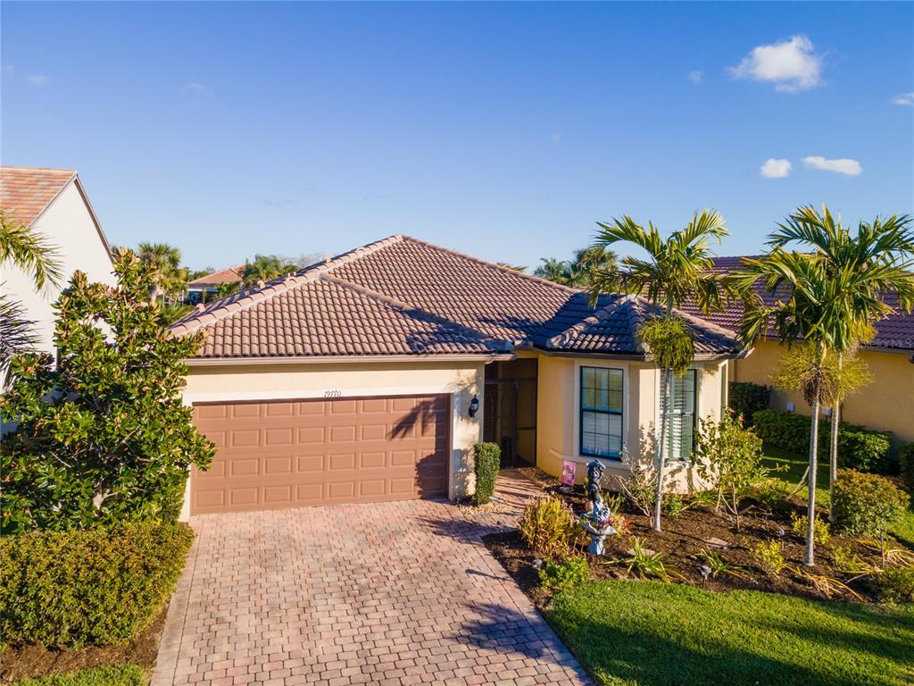 A yellow stucco house features a brown garage door, a screened entryway, and a garden — 19770 QUISTO STREET, VENICE, FL
