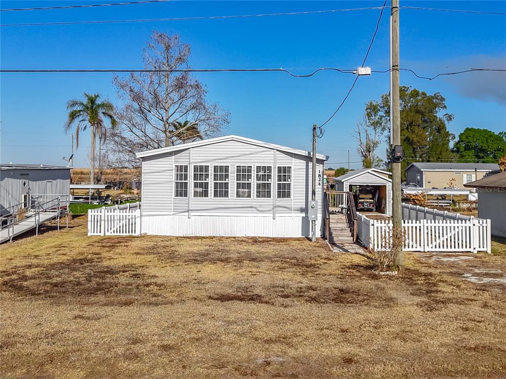 A light-colored manufactured home with a white picket fence and a detached garage — 1824 RIVERSIDE DRIVE, MOORE HAVEN, FL