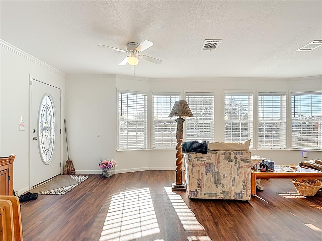 A living room features wood-look flooring, a ceiling fan, and a bay window with blinds — 1824 RIVERSIDE DRIVE, MOORE HAVEN, FL