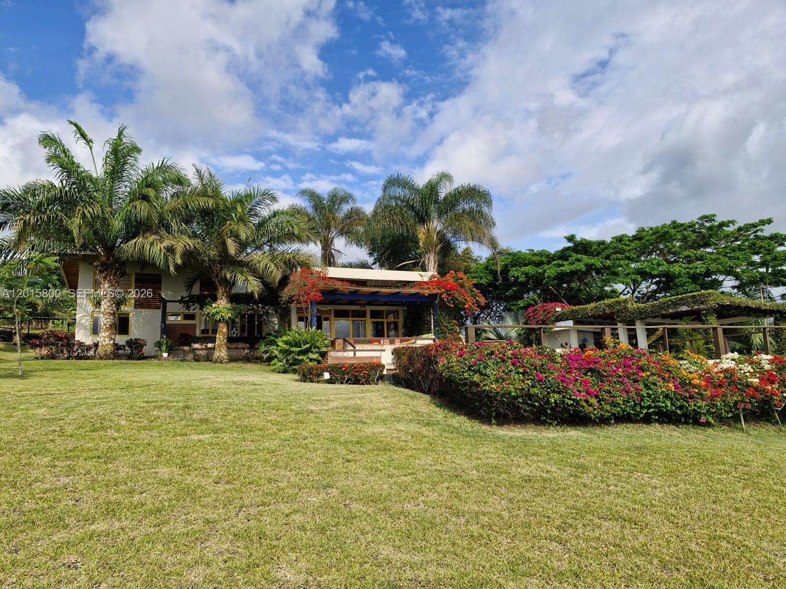 A two-story house with palm trees and a flowering garden sits on a grassy lawn — San Jose San Jose, FL