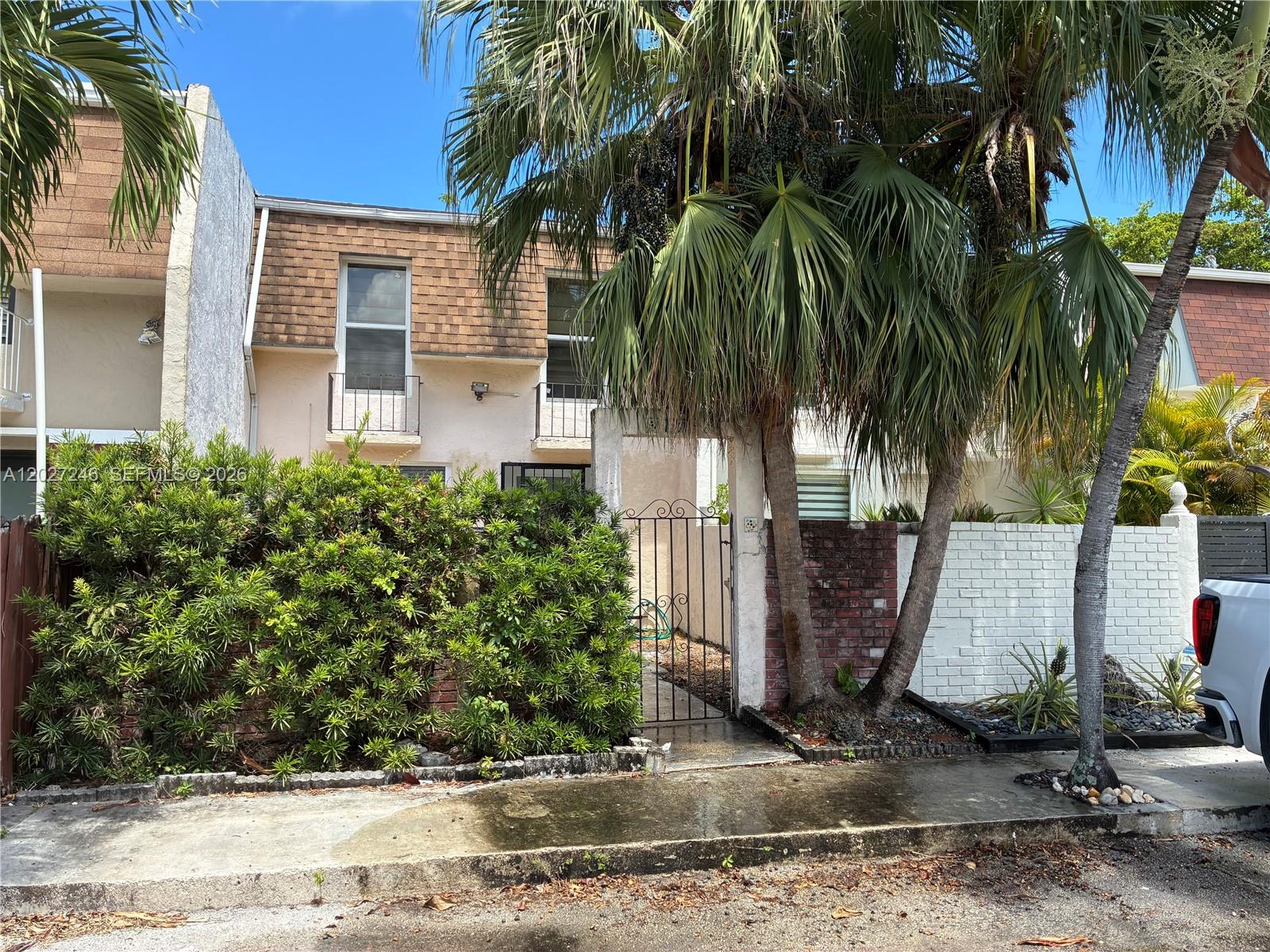 A two-story townhouse exterior features a gated courtyard, palm trees, and a brick wall — 13509 NE 24th Pl, North Miami FL 33181, NORTH MIAMI, FL