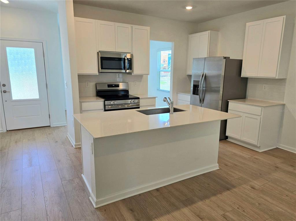A kitchen features white cabinets, stainless steel appliances, and a central island with quartz countertops — 4346 BENTGRASS BEND, ST CLOUD, FL