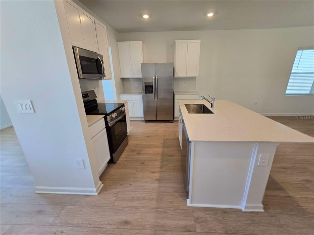 A kitchen features white cabinets, stainless steel appliances, a center island, and light wood flooring — 4346 BENTGRASS BEND, ST CLOUD, FL
