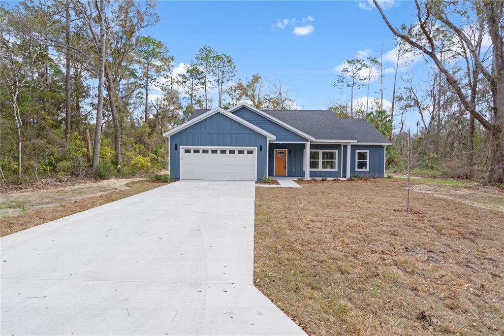 A blue, single-story house with a white garage door sits on a wooded lot — 11231 NW 92ND CT, CHIEFLAND, FL