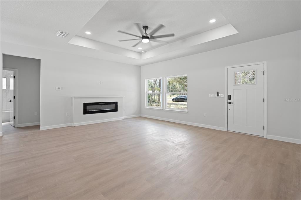 A living room features light wood-look flooring, a tray ceiling with a fan, and a fireplace — 11231 NW 92ND CT, CHIEFLAND, FL