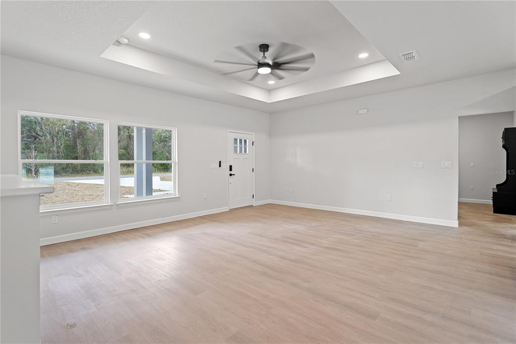 A spacious living room features light wood flooring, a tray ceiling with a fan, and windows — 11231 NW 92ND CT, CHIEFLAND, FL