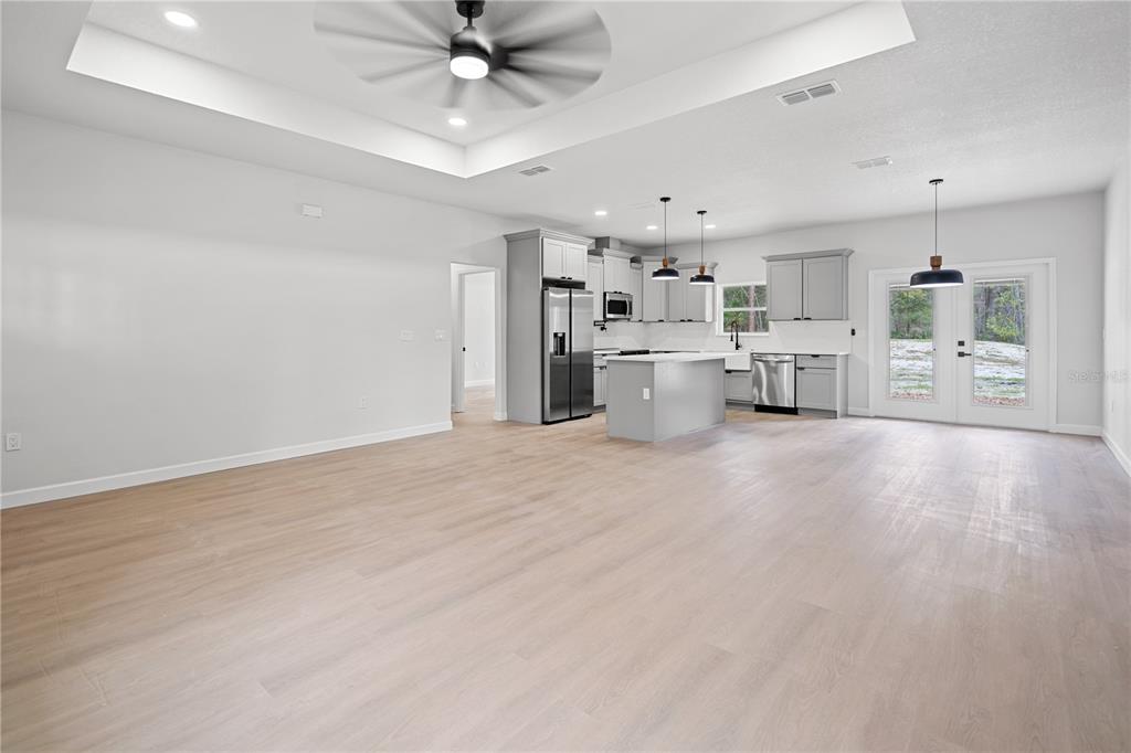 An open-concept kitchen and living area feature light wood flooring, gray cabinetry, and recessed lighting — 11231 NW 92ND CT, CHIEFLAND, FL