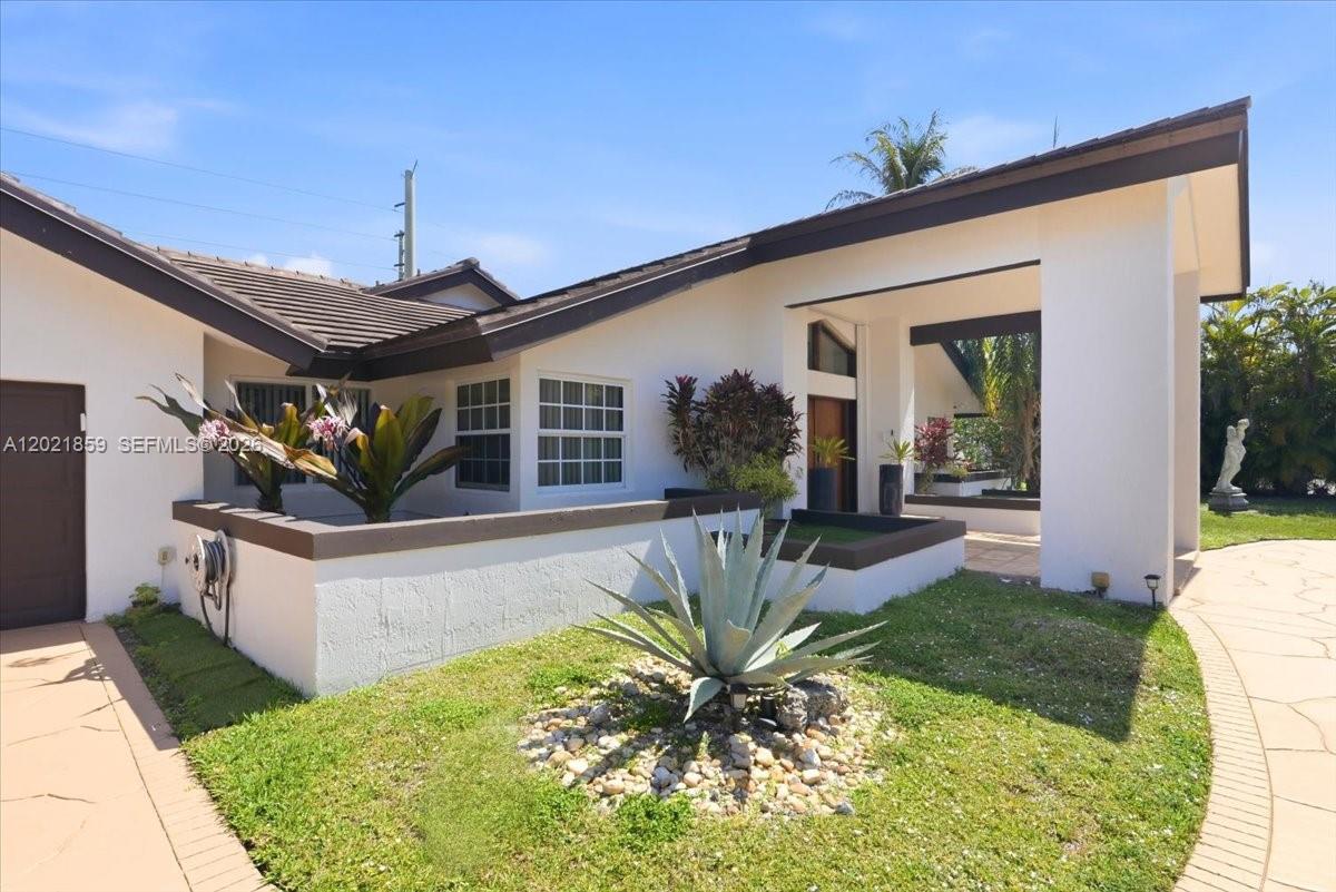 The exterior of a white house features a covered entryway, a small garden, and a walkway — 9665 SW 136th St, Miami FL 33176, MIAMI, FL