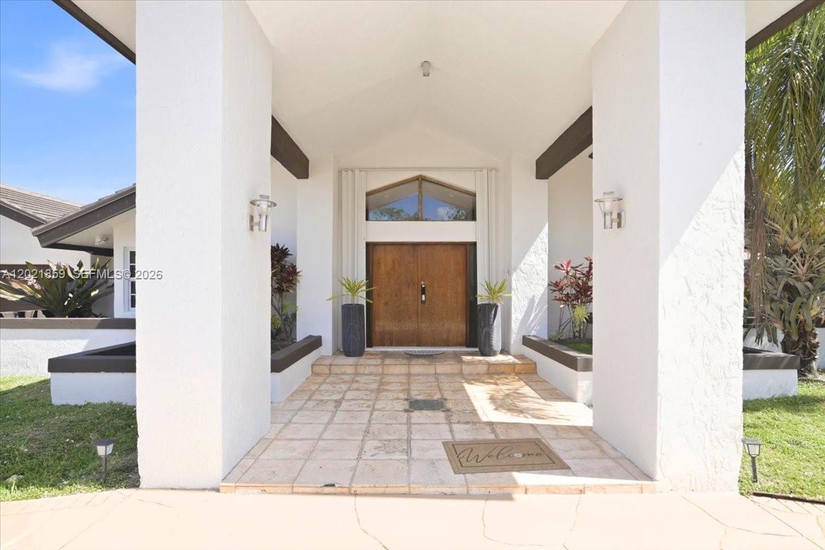 A covered entryway features a double wood door, tiled floor, and white stucco columns — 9665 SW 136th St, Miami FL 33176, MIAMI, FL