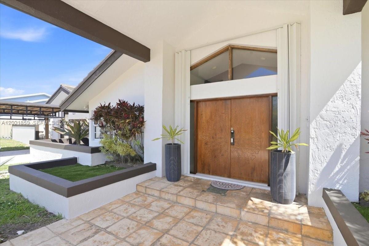 A double wooden door with carved details serves as the entrance to a tiled patio — 9665 SW 136th St, Miami FL 33176, MIAMI, FL