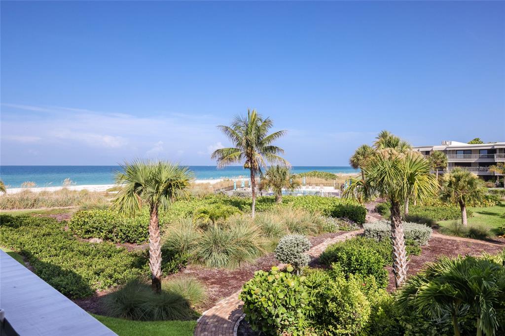 A view of a tropical beach and ocean from a balcony overlooking landscaped grounds — 5757 GULF OF MEXICO DRIVE UNIT 205, LONGBOAT KEY, FL