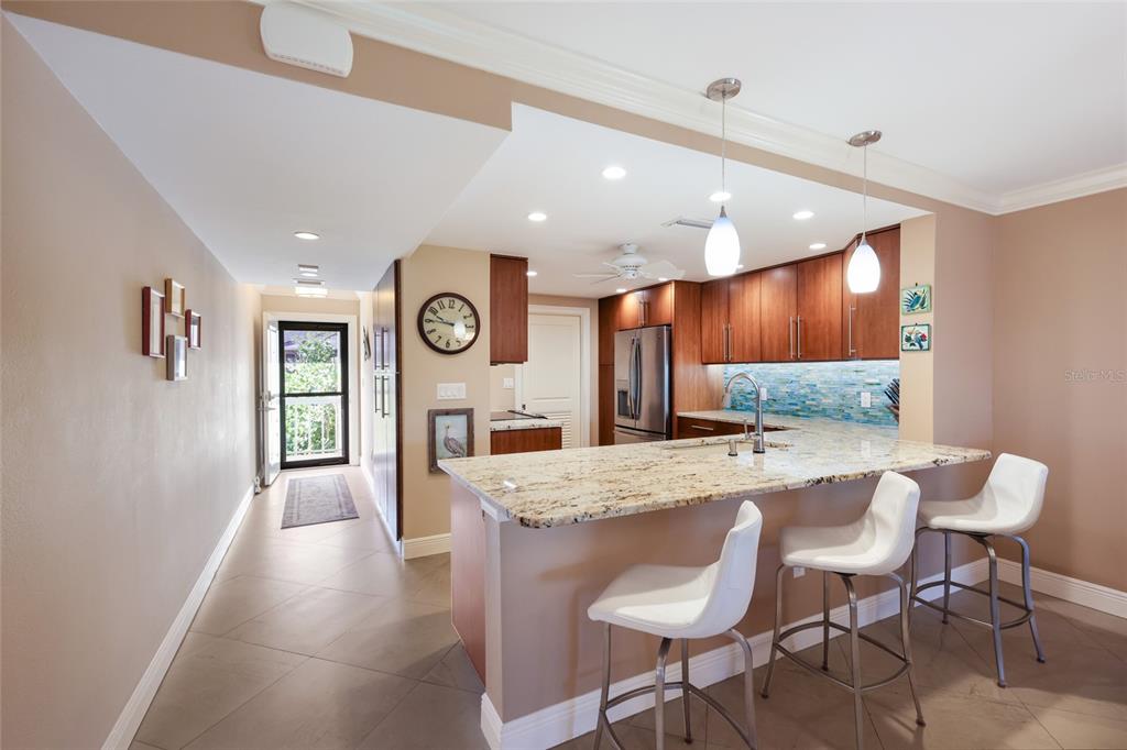 A kitchen with granite countertops, wooden cabinets, and three white bar stools on tile flooring — 5757 GULF OF MEXICO DRIVE UNIT 205, LONGBOAT KEY, FL