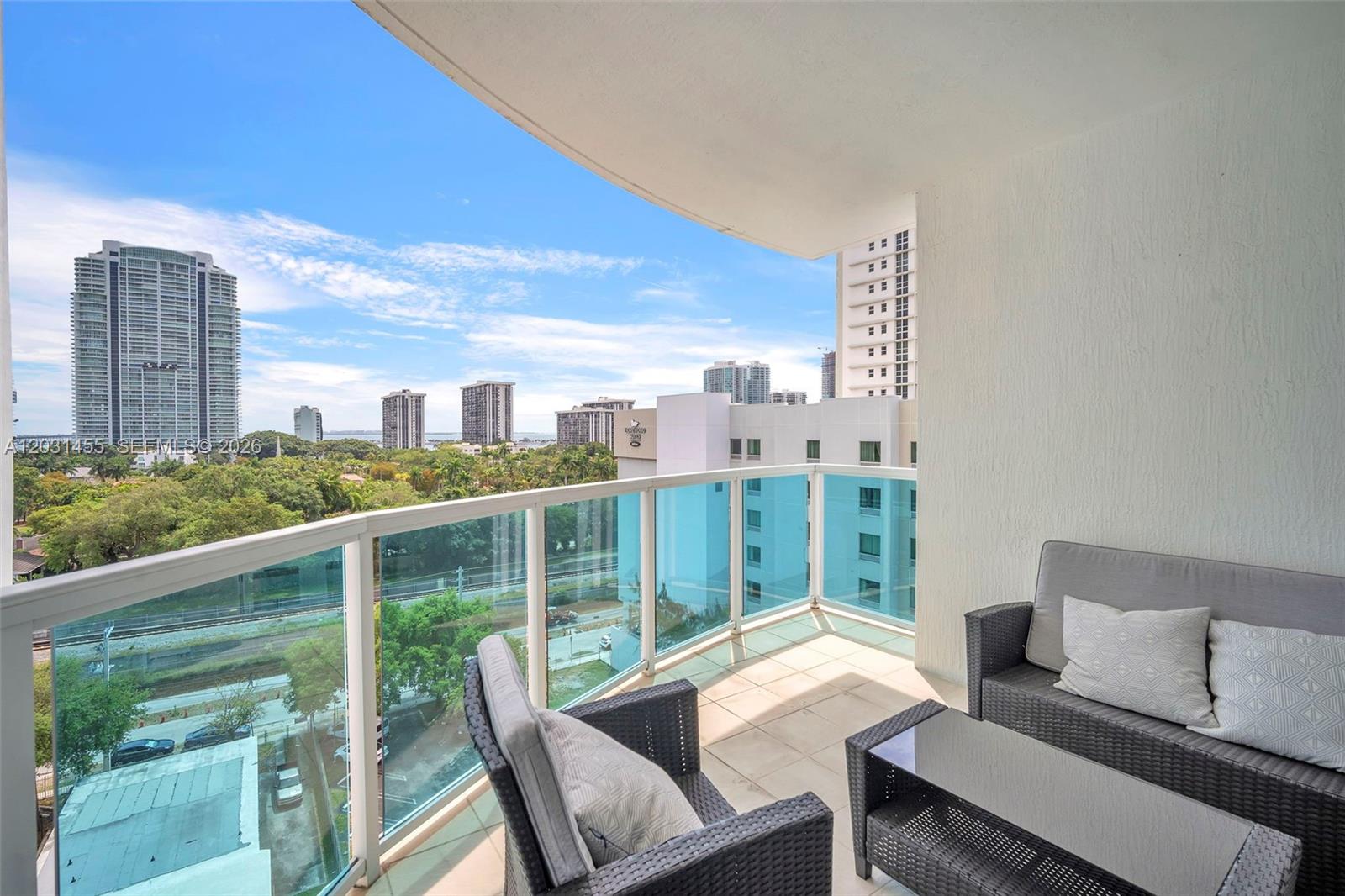 A balcony with wicker furniture overlooks a city skyline and green trees — 1723 SW 2nd Ave # 1001, Miami FL 33129, MIAMI, FL