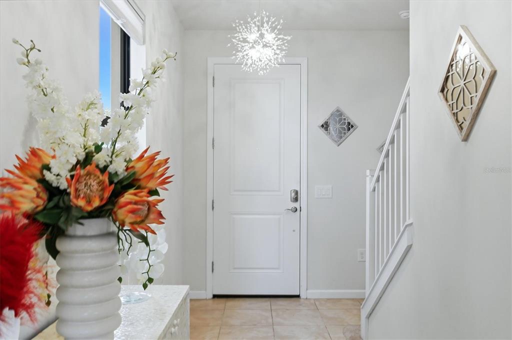 An entryway features a white door, a modern chandelier, and a staircase with white railings — 6126 BLUESTAR COURT, LAKEWOOD RANCH, FL