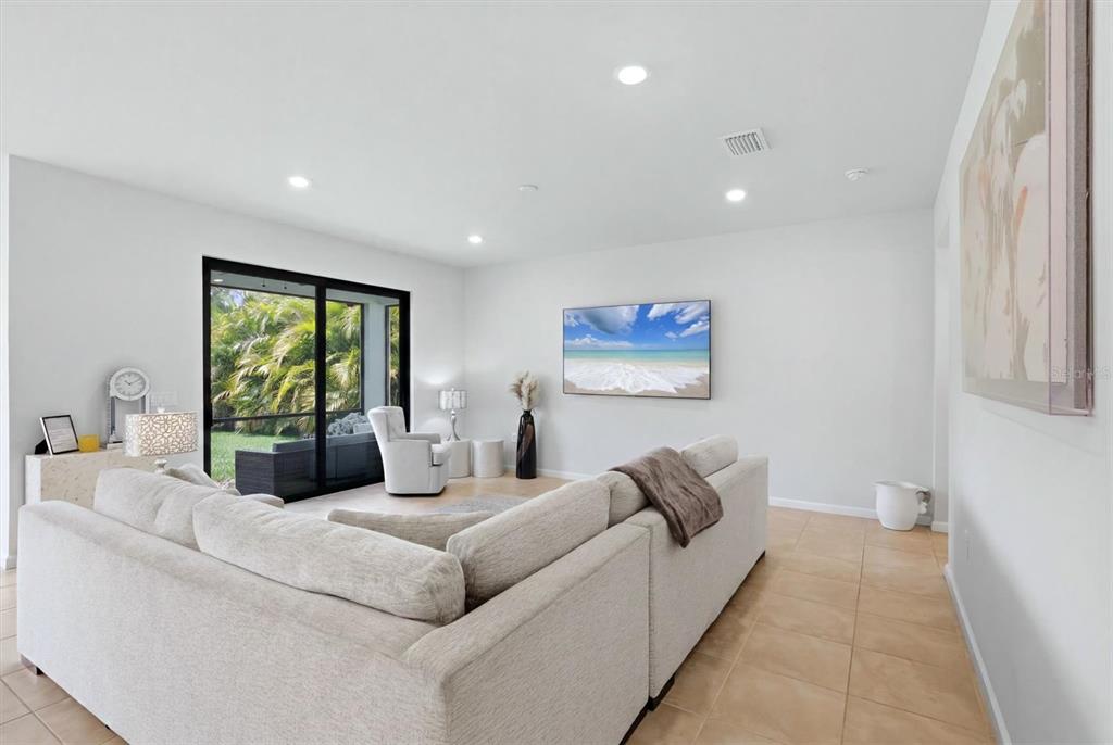 A living room features a beige sectional sofa, a wall-mounted television, and sliding glass doors — 6126 BLUESTAR COURT, LAKEWOOD RANCH, FL