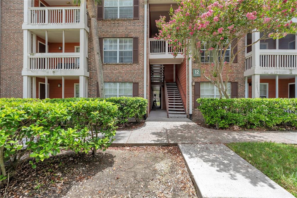 A brick apartment building exterior features a central staircase, screened balconies, and landscaped bushes — 10200 GANDY BOULEVARD N UNIT 1205, ST PETERSBURG, FL