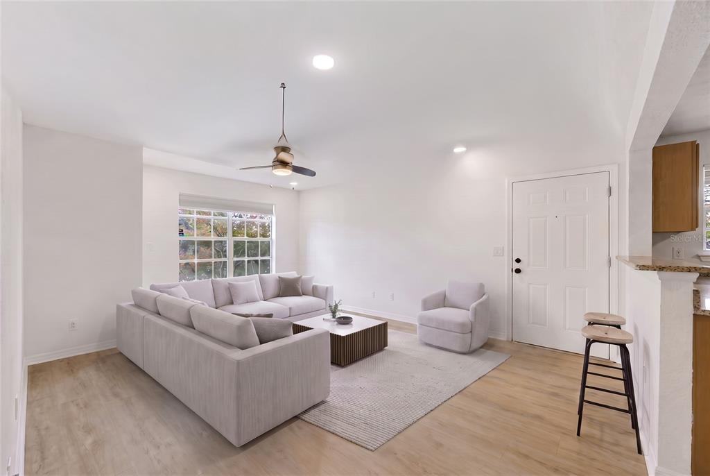 A living room features light wood flooring, a sectional sofa, an armchair, and a ceiling fan — 10200 GANDY BOULEVARD N UNIT 1205, ST PETERSBURG, FL