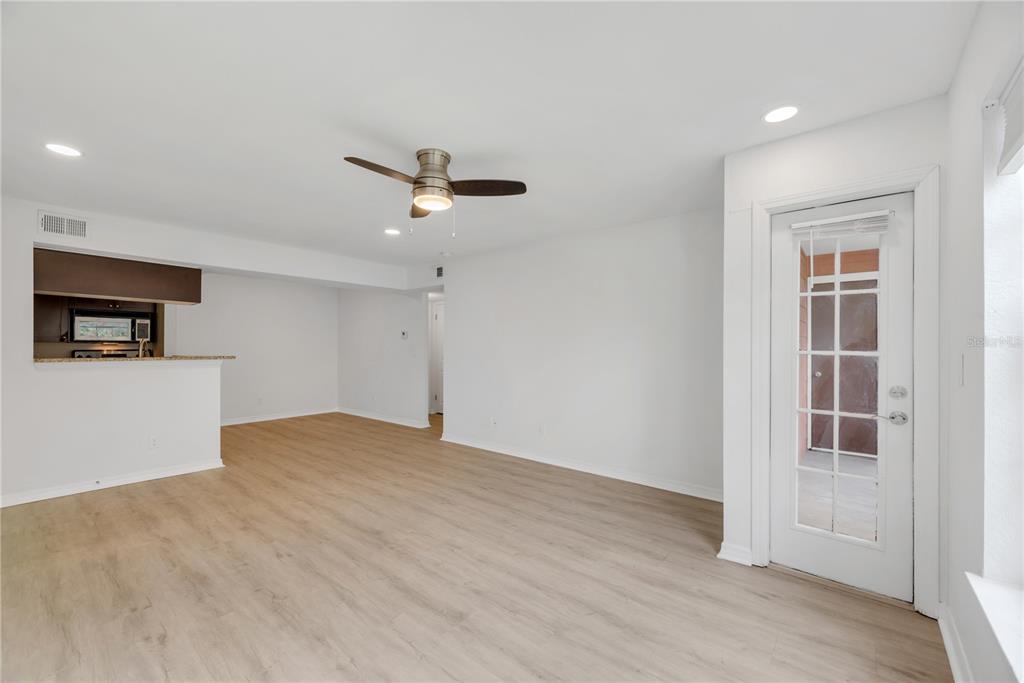 An open-concept living area features light wood-look flooring, a ceiling fan, and a glass-paneled door — 10200 GANDY BOULEVARD N UNIT 1205, ST PETERSBURG, FL