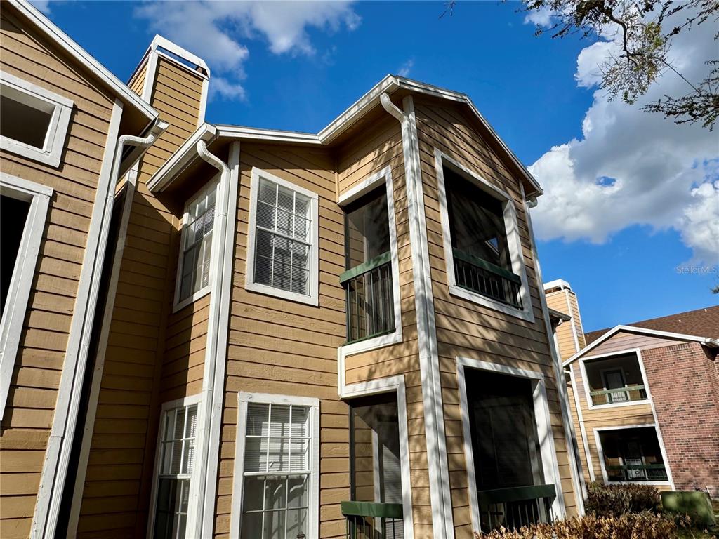 A low-angle exterior view of a two-story tan building with screened balconies and white trim — 5533 CHRISHIRE WAY UNIT F207, ORLANDO, FL