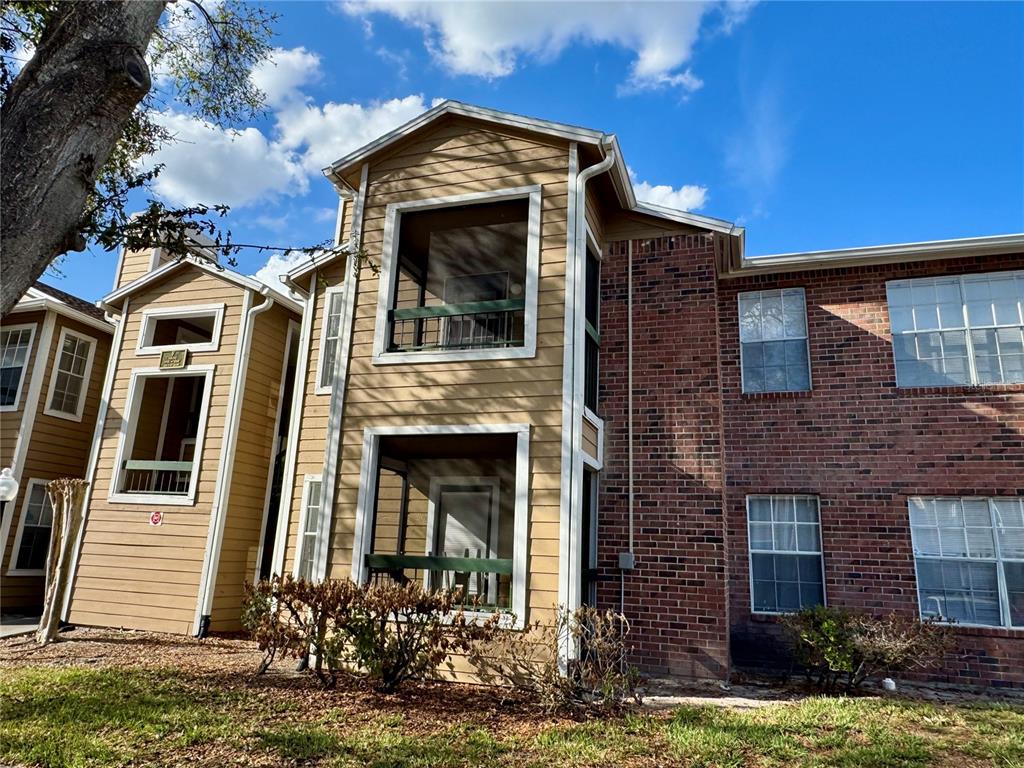 The exterior of a two-story apartment building features tan siding, brick accents, and screened balconies — 5533 CHRISHIRE WAY UNIT F207, ORLANDO, FL