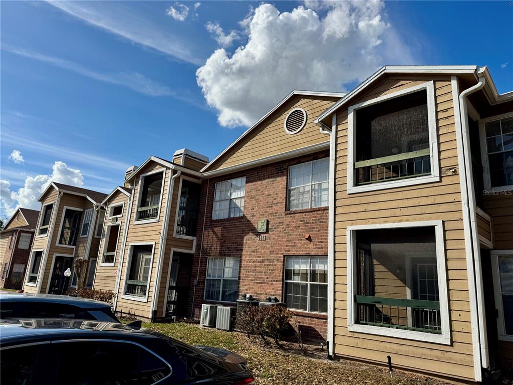 A multi-story apartment building exterior features brick siding, tan horizontal siding, and screened-in balconies — 5533 CHRISHIRE WAY UNIT F207, ORLANDO, FL