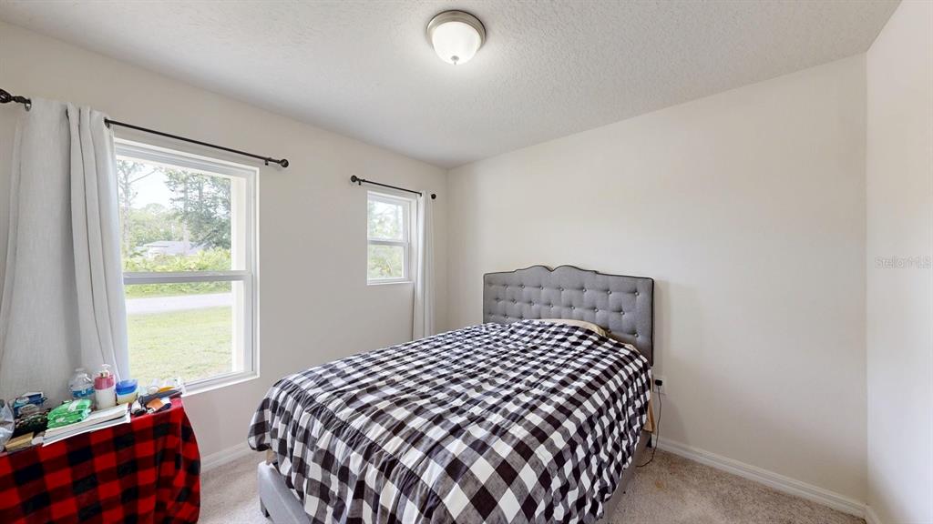 A bedroom features a bed with a plaid comforter, two windows, and a ceiling light — 173 RYBERRY DRIVE, PALM COAST, FL