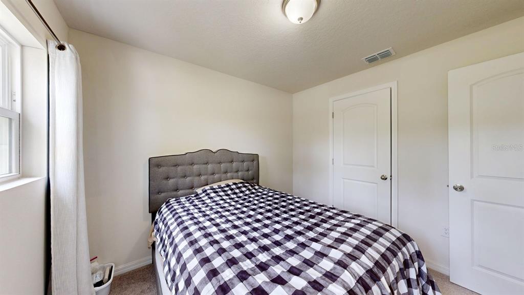 A bedroom features a bed with a plaid comforter, two white doors, and beige carpet — 173 RYBERRY DRIVE, PALM COAST, FL