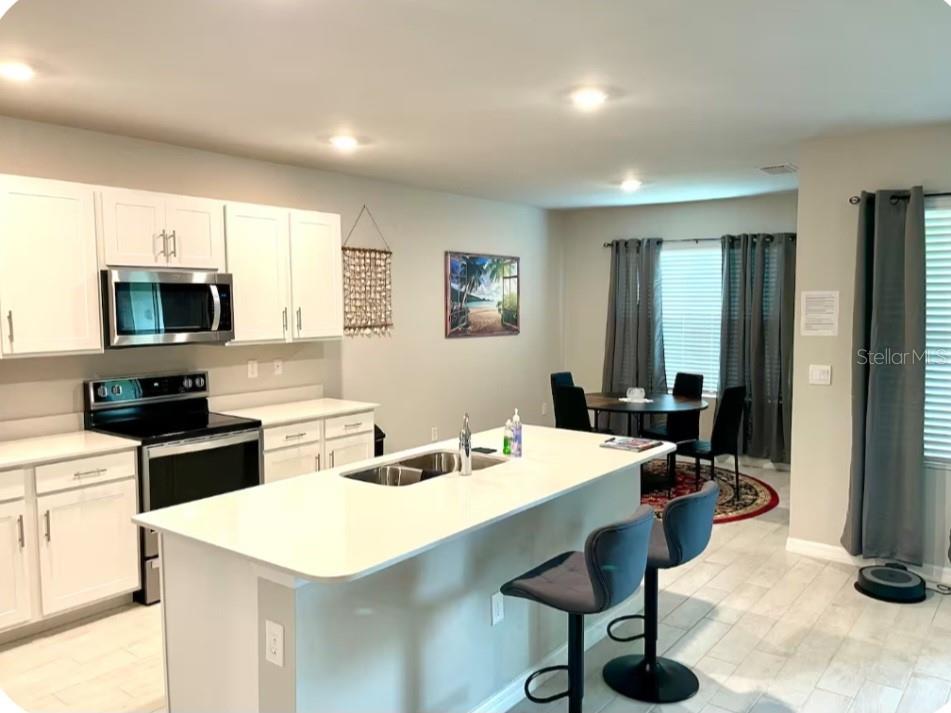 A kitchen with white cabinets, a central island, and an adjacent dining area with curtains — 25336 DEEP CREEK BOULEVARD, PUNTA GORDA, FL