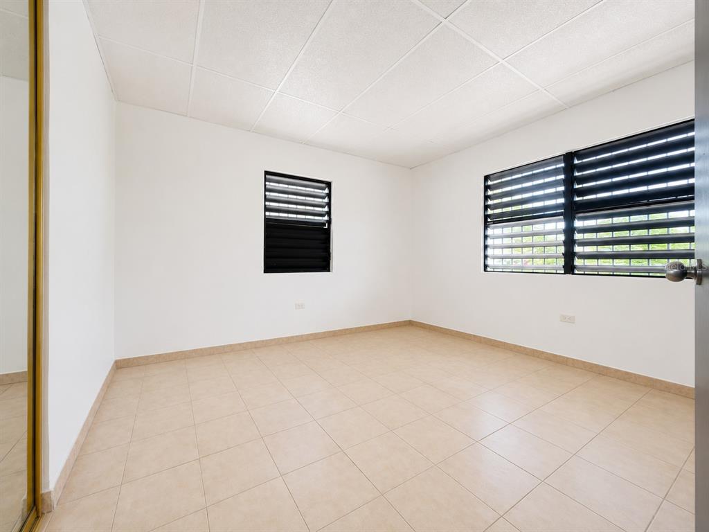 An empty bedroom features white walls, light-colored tile flooring, and two windows with black louvers — #1 ST. URB. VILLA ARRIETA 2ND FLOOR UNIT C-51, BAYAMON, PR