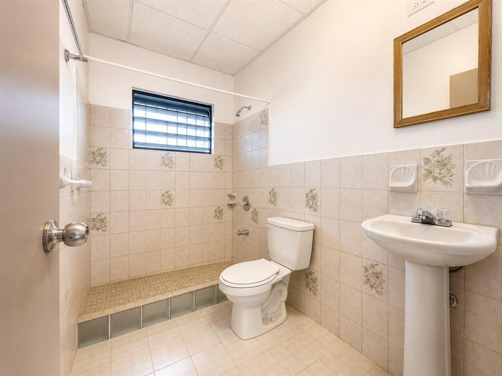 A bathroom features a walk-in shower, a pedestal sink, a toilet, and beige tiled walls — #1 ST. URB. VILLA ARRIETA 2ND FLOOR UNIT C-51, BAYAMON, PR