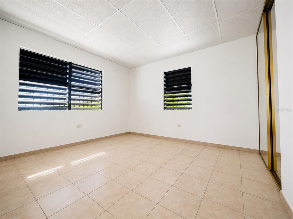 An empty room features white walls, tan tile flooring, a drop ceiling, and louvered windows — #1 ST. URB. VILLA ARRIETA 2ND FLOOR UNIT C-51, BAYAMON, PR